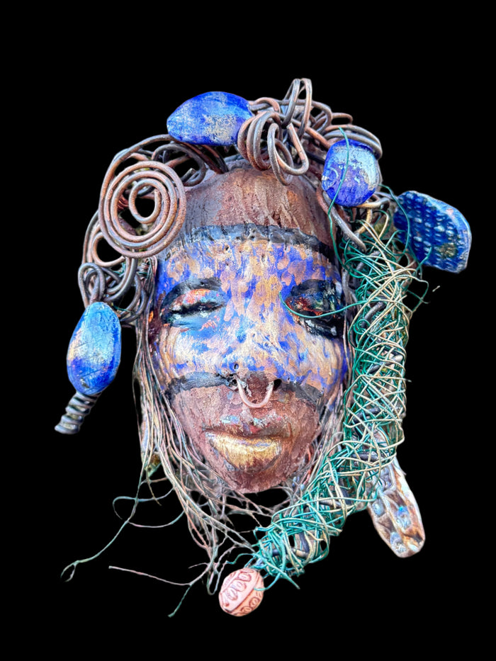 Introducing Monifa, a 4 x 6" mixed media raku fire mask that exquisitely blends a beautiful design with 24 and 16 gauge wire, intricate blue tribal beads, and over 15 feet of wire. Display it with pride on a solid black or white background, or for a more stunning look, try it against a backdrop of lush, mossy trees.