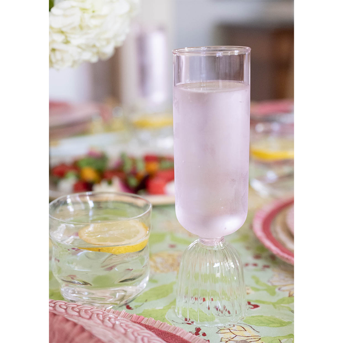 Tall clear glass pink champagne flute with ribbed base filled with cold liquid.