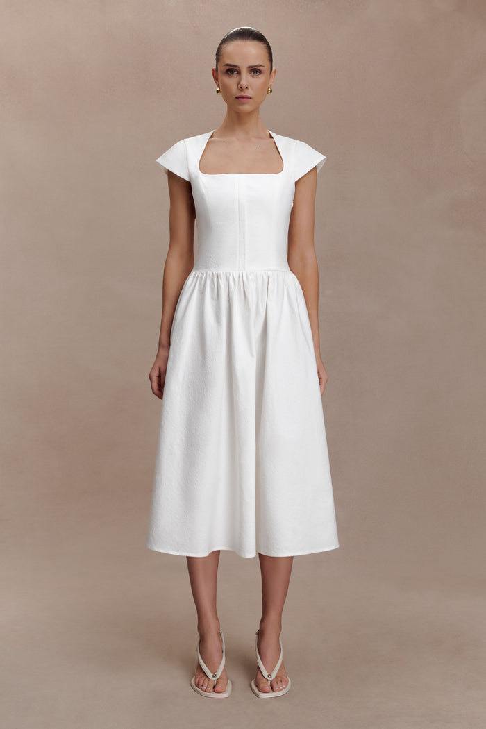 Woman wearing a white dress against a beige background