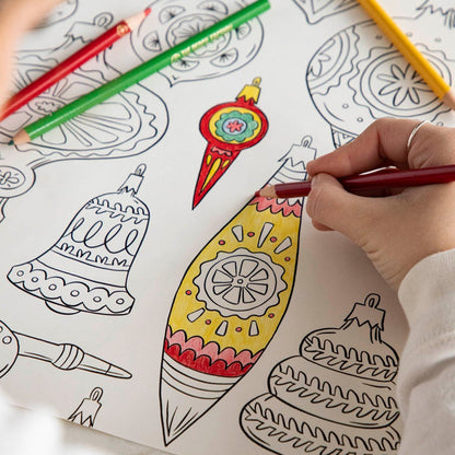A woman coloring an ornament on the Christmas Coloring Placemat with scattered colored pencils.