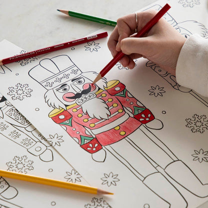 A woman coloring a nutcracker on the Christmas Coloring Placemat with scattered colored pencils.