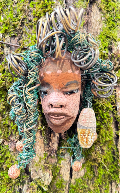 Davina is a 4” x 5” 5oz. mixed media raku fire mask made with 20 feet of 24 and 16 gauge wire. It boasts a striking, three-colored design and includes a large Raku fired earring with wooden beads. This unique piece is the perfect addition to your HerDew mask collection. Experience the enhanced beauty of Davina when paired with tree bark.