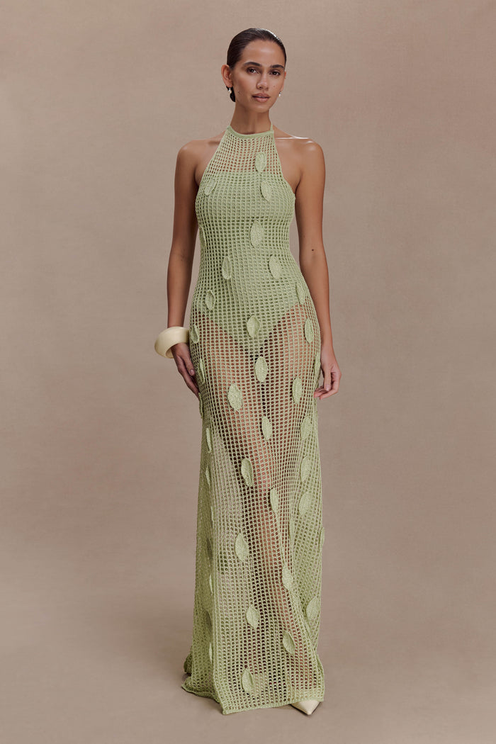 Woman wearing a sheer green crochet halter maxi dress with intricate leaf detailing.