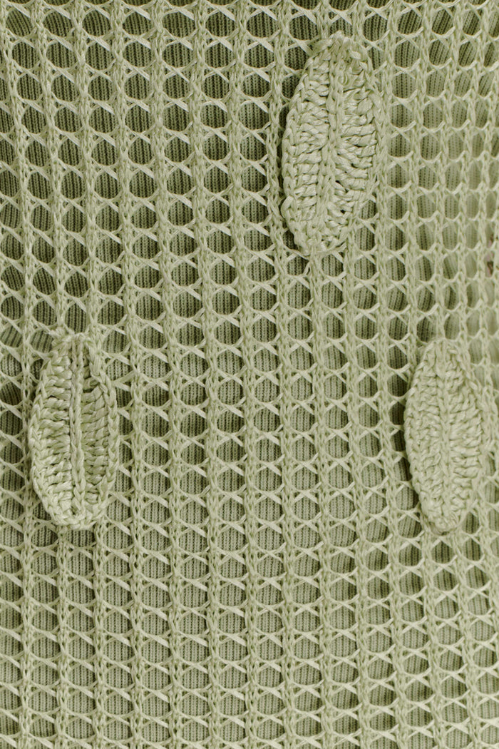 Close-up of a textured green crochet fabric with leaf detailing.