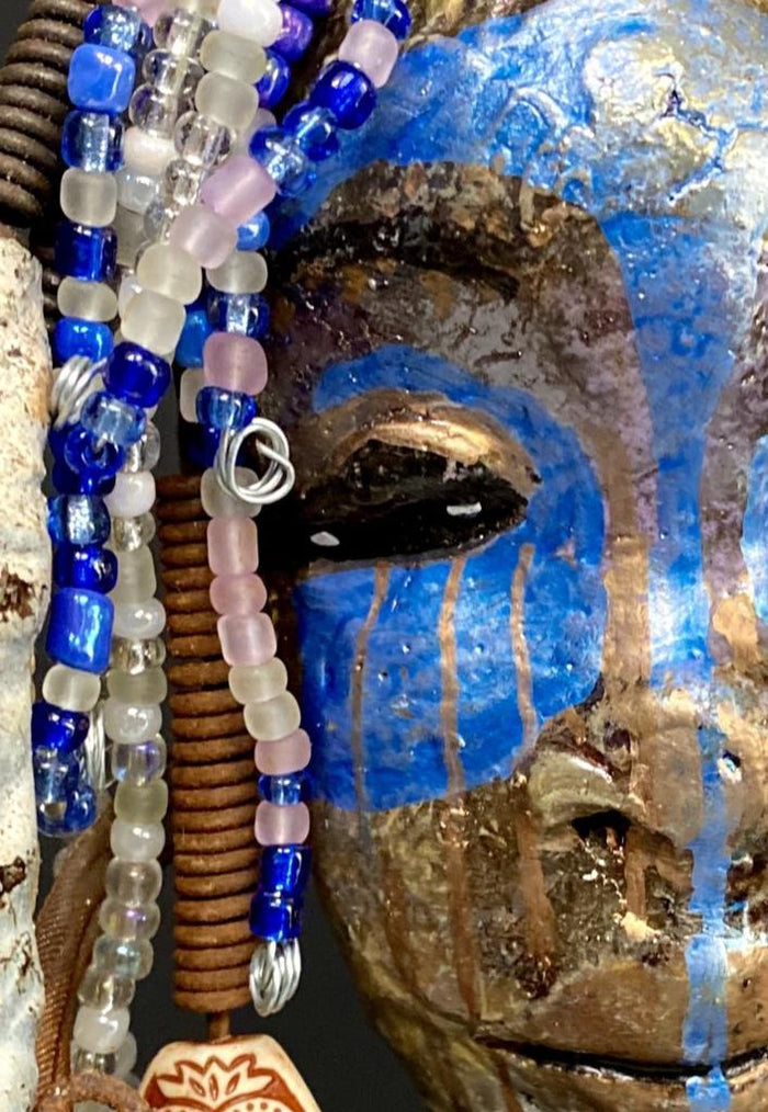 I started making mask soon after seeing authentic African artwork at the Smithsonian Museum of African Art. I was in total awe. I was inspired by my visit there..  Haze has a multi colored blue tone  metallic copper complexion. She is 7" x 5" and weighs 10 ozs. Haze  has  over 50 mini beads and handmade raku beads. Haze has over 4 feet of 16 gauge wire hair.