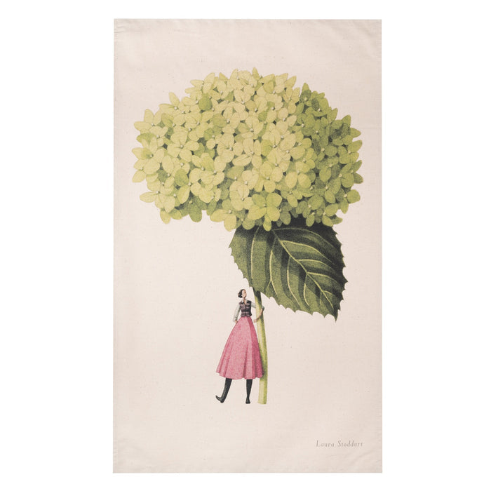 A tan tea towel featuring a stylized illustration of a woman in a pink skirt holding a gigantic green hydrangea bloom by the stem.