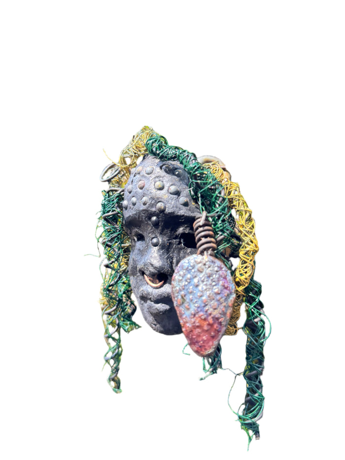 Enhance your HerDew mask collection with Kao! This mixed media raku fire mask is 4” x 6” and 6oz., featuring 25 feet of 24 and 16 gauge wire and a copper nose ring. Its exotic appeal is captured in a photo on tree bark, adding a unique touch to your collection. The mask's Smokey black complexion and Raku fired earring with a wooden bead make it a truly stunning piece..
