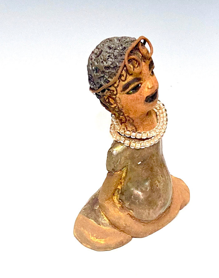 Meet karisha! Karisha stands 6" x 4" x 3" and weighs 8.7 ozs.  Karisha has a lovely glossy green dress with a matching hat.  She has curly wire hair.  Karisha appears to sit in a yoga pose. Her long arms rest at her side. Karisha is a great starter piece from the Herdew Collection!