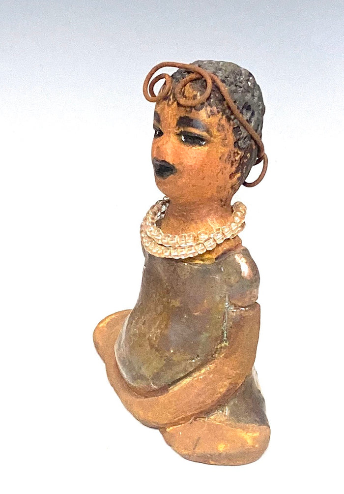 Meet karisha! Karisha stands 6" x 4" x 3" and weighs 8.7 ozs.  Karisha has a lovely glossy green dress with a matching hat.  She has curly wire hair.  Karisha appears to sit in a yoga pose. Her long arms rest at her side. Karisha is a great starter piece from the Herdew Collection!