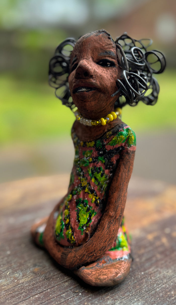 Introducing Katie, the fearless figurine who measures 6" x 4" x 3" and weighs a mere 11 ozs. Donning a stunning speckled red and green dress and with her coiled hair as her crown of glory, Katie exudes confidence and courage as she sits in a yoga pose, exuding curiosity. Begin your journey with the Herdew Collection and experience the thrill of free shipping and our customer-friendly return policy. Don't miss out on this one-of-a-kind piece!