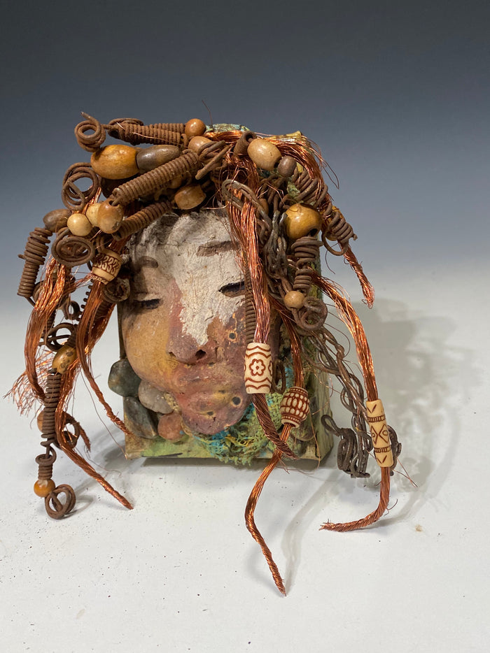 I started making art soon after seeing authentic African artwork at the Smithsonian Museum of African Art. I was in total awe. Lulu was inspired by my visit there.  Lulu is uniquely mounted on a painted 6"x 4"x 2" canvas. It weighs 1.15 lbs. Her face has a two tone off white  and earthy crackle glaze. Lulu has hand coiled wire, white and multi color beads, textured earthy cloth..
