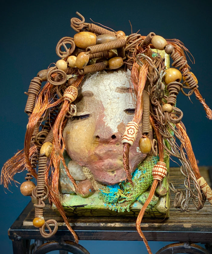 I started making art soon after seeing authentic African artwork at the Smithsonian Museum of African Art. I was in total awe. Lulu was inspired by my visit there.  Lulu is uniquely mounted on a painted 6"x 4"x 2" canvas. It weighs 1.15 lbs. Her face has a two tone off white  and earthy crackle glaze. Lulu has hand coiled wire, white and multi color beads, textured earthy cloth..