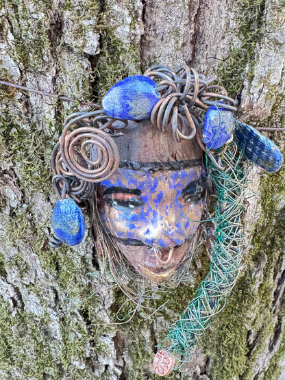 Introducing Monifa, a 4 x 6" mixed media raku fire mask that exquisitely blends a beautiful design with 24 and 16 gauge wire, intricate blue tribal beads, and over 15 feet of wire. Display it with pride on a solid black or white background, or for a more stunning look, try it against a backdrop of lush, mossy trees.