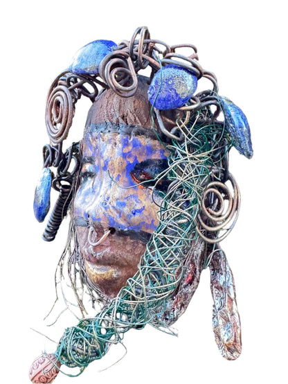 Introducing Monifa, a 4 x 6" mixed media raku fire mask that exquisitely blends a beautiful design with 24 and 16 gauge wire, intricate blue tribal beads, and over 15 feet of wire. Display it with pride on a solid black or white background, or for a more stunning look, try it against a backdrop of lush, mossy trees.