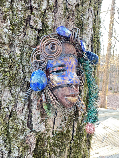 Introducing Monifa, a 4 x 6" mixed media raku fire mask that exquisitely blends a beautiful design with 24 and 16 gauge wire, intricate blue tribal beads, and over 15 feet of wire. Display it with pride on a solid black or white background, or for a more stunning look, try it against a backdrop of lush, mossy trees.