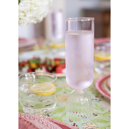 Tall clear glass pink champagne flute with ribbed base filled with cold liquid.