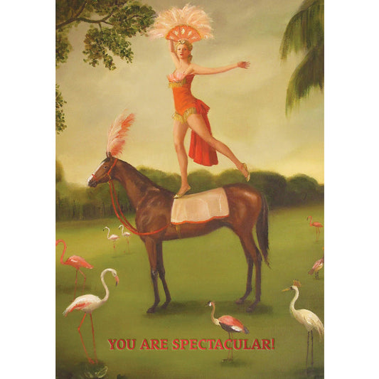 A painterly illustration of a showgirl in a coral costume with a pink feathery headdress balancing on one foot on the back of a brown circus horse dressed to match. The scene takes place on a green lawn with trees in the background, surrounded by pink flamingos. The message "YOU ARE SPECTACULAR!" is printed in red across the bottom of the card.